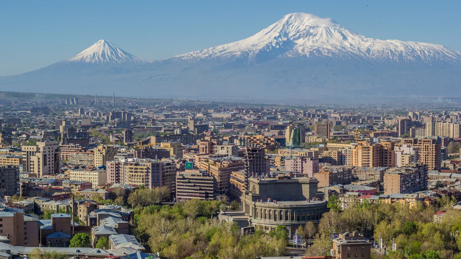 Yerevan's skyline with the Opera House among green trees and snow-capped Mount Ararat on the horizon