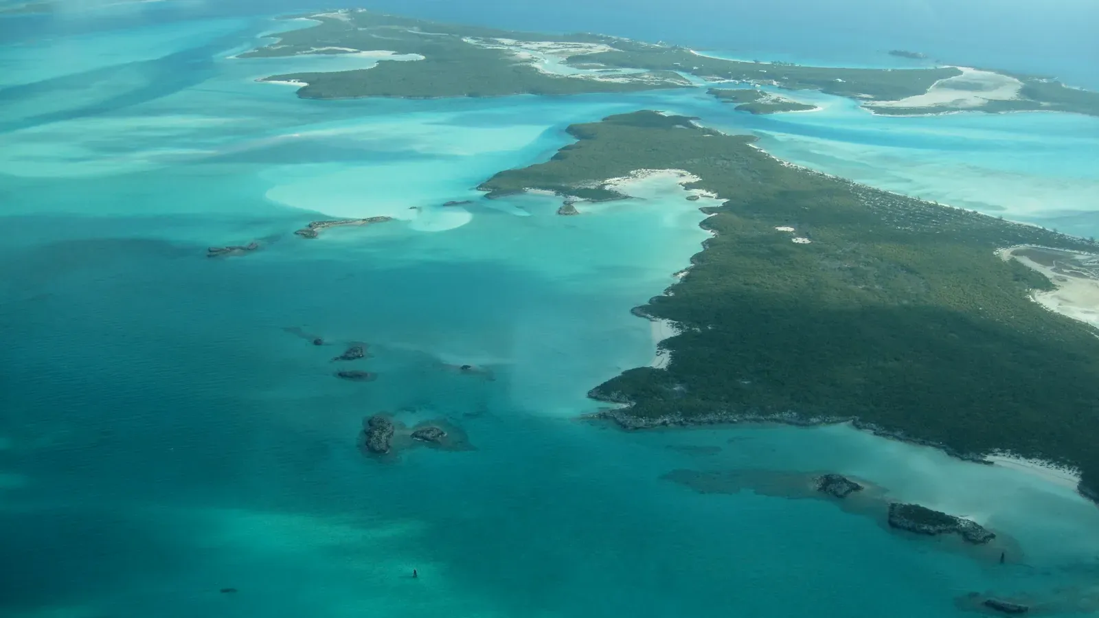 Low green islands in shallow turquoise water, seen from the air over The Bahamas