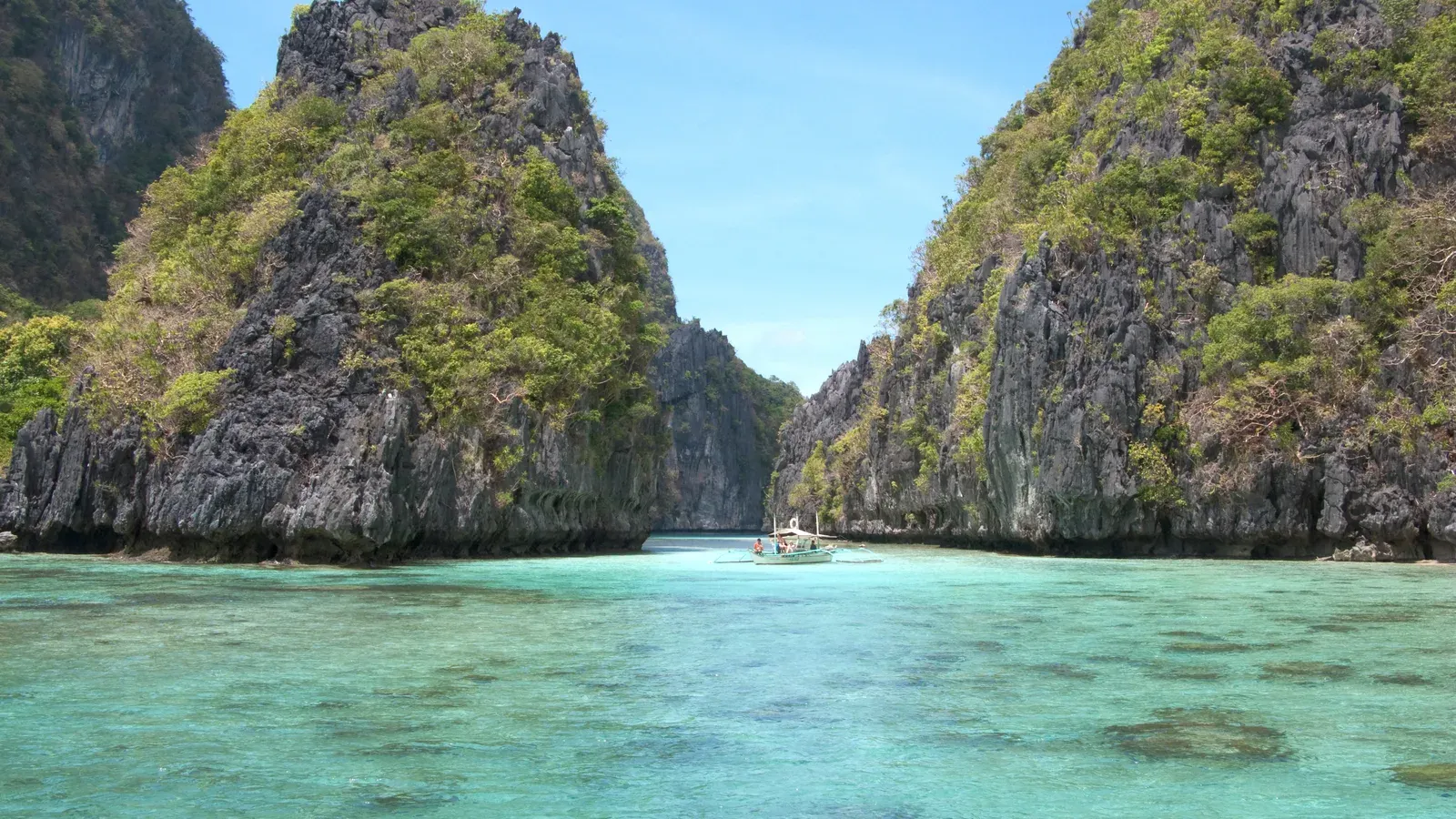 Limestone karst cliffs around a turquoise lagoon with a small outrigger boat in Bacuit Bay, El Nido, Palawan, Philippines