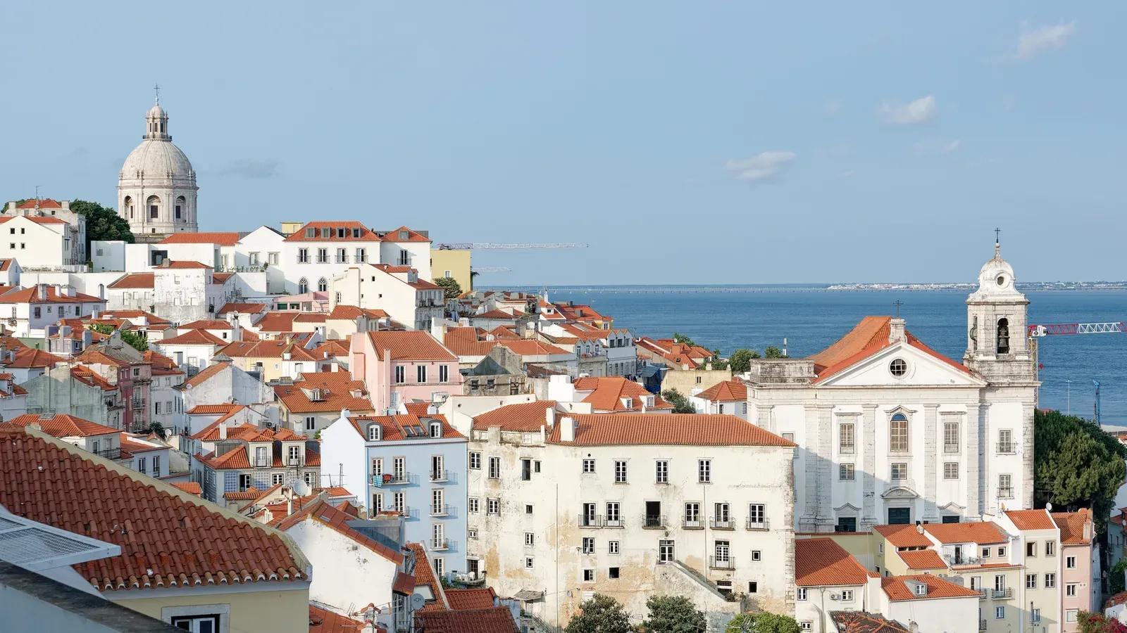 Red-tiled roofs of Lisbon's Alfama district from Miradouro de Santa Luzia, with the dome of Santa Engrácia and the Tagus River beyond, Portugal